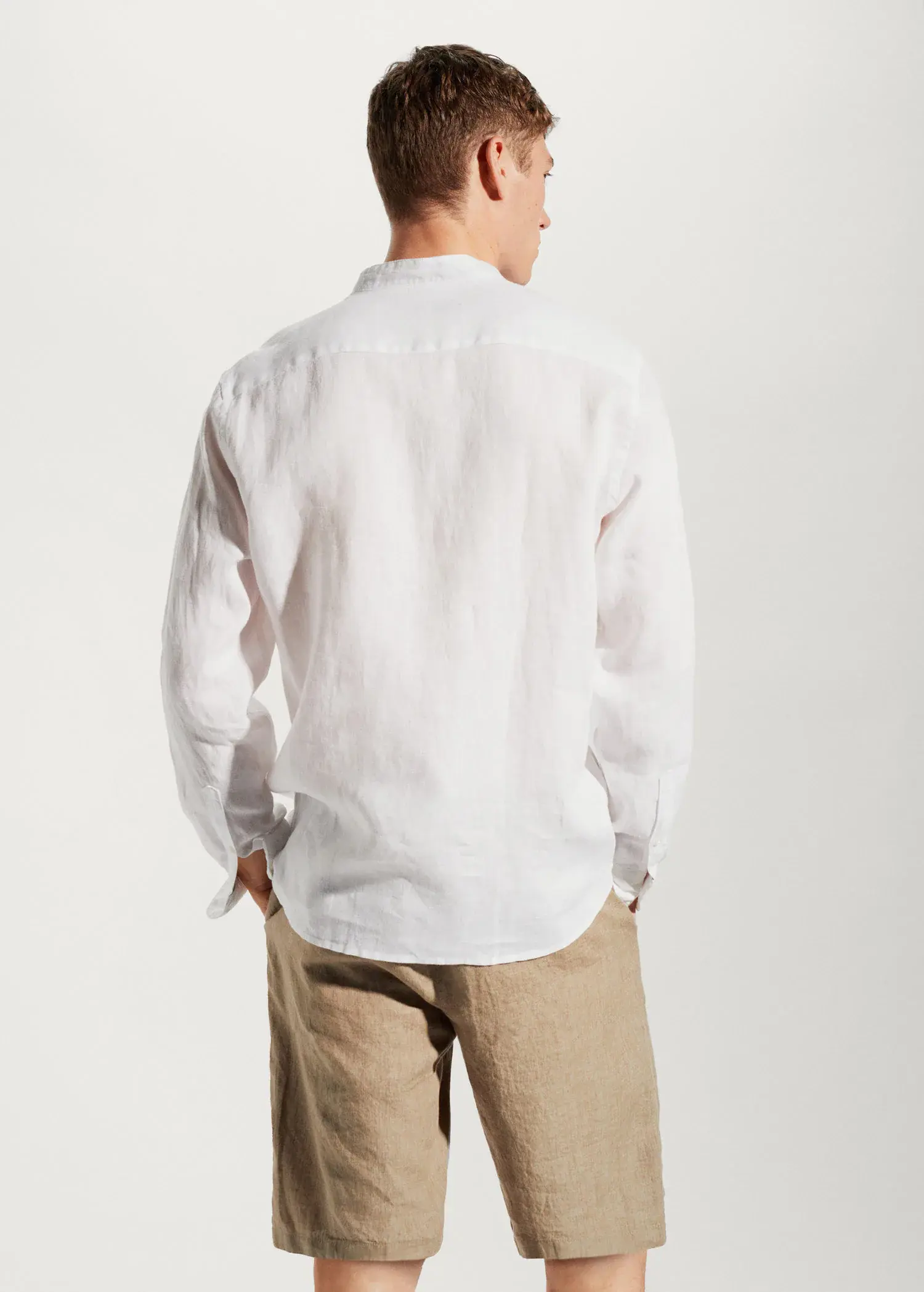 Mango 100% linen Mao collar shirt. a man in a white shirt is standing with his hands in his pockets. 
