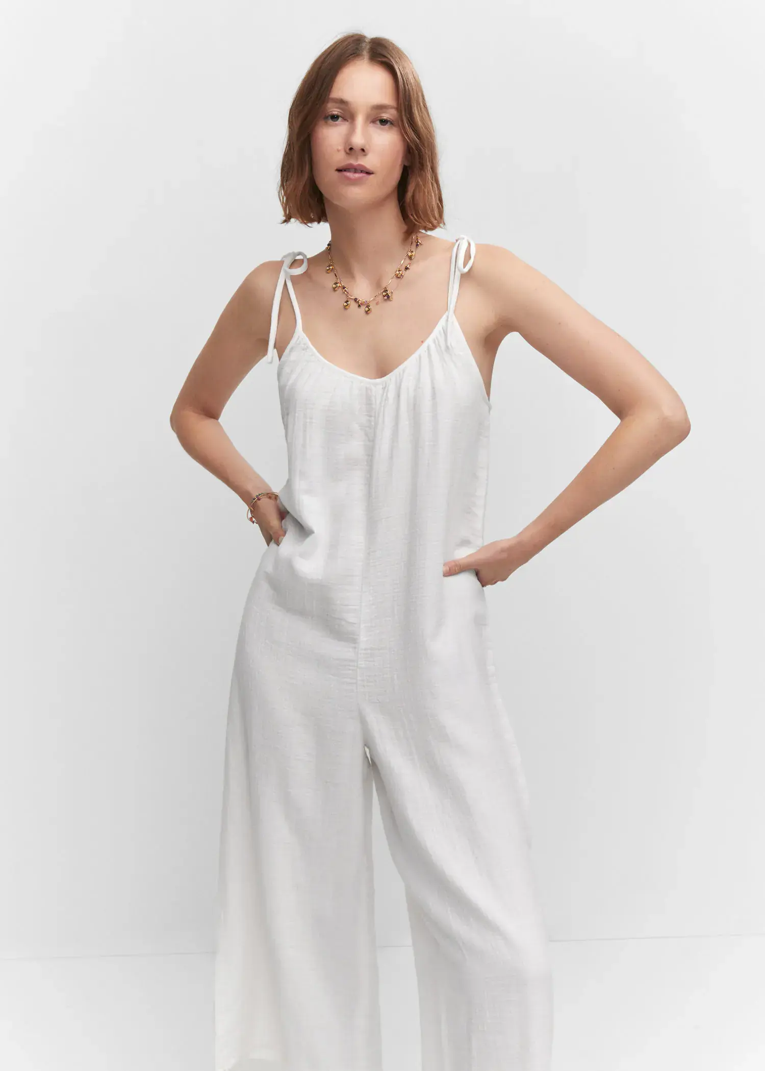 Mango Textured jumpsuit with bows. a woman wearing a white jumpsuit posing for a picture. 