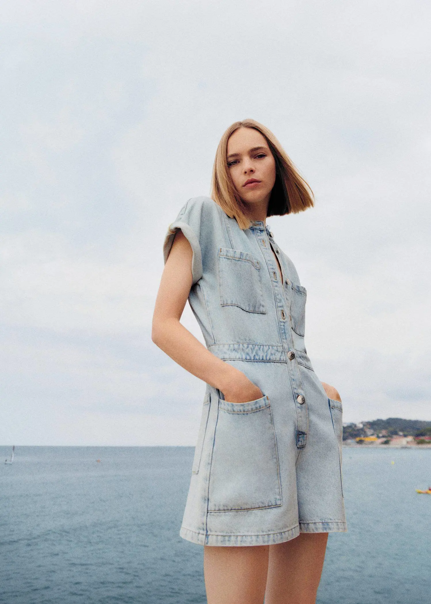 Mango Denim jumpsuit with pockets. a woman standing in front of a body of water 