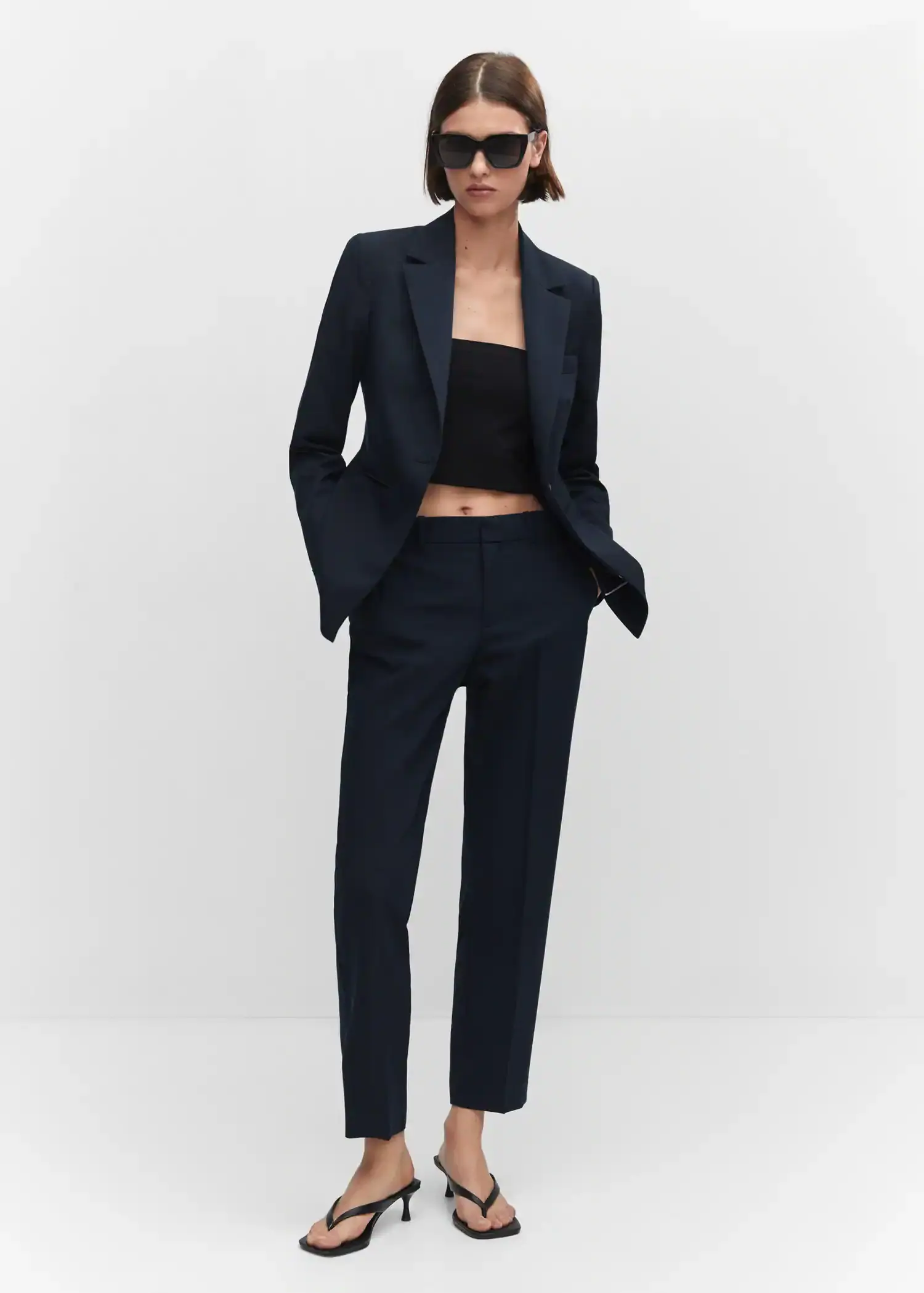 Mango Fitted suit jacket. a woman in a black suit stands in front of a white wall. 