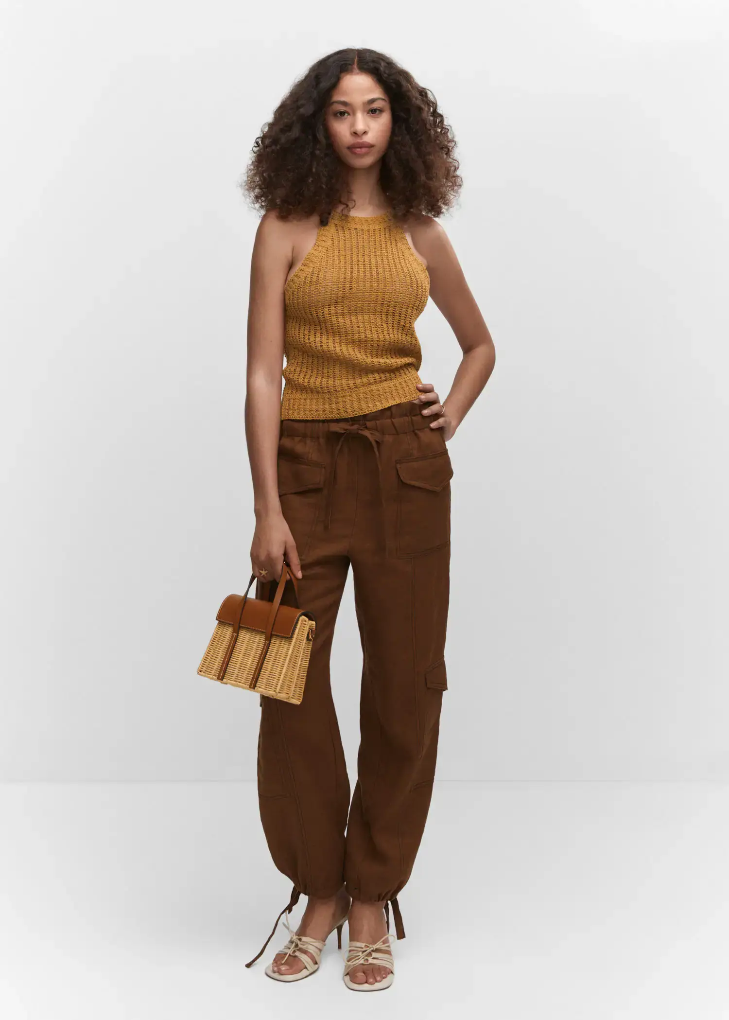 Mango Halter-neck knitted top. a woman standing in front of a white wall holding a purse. 