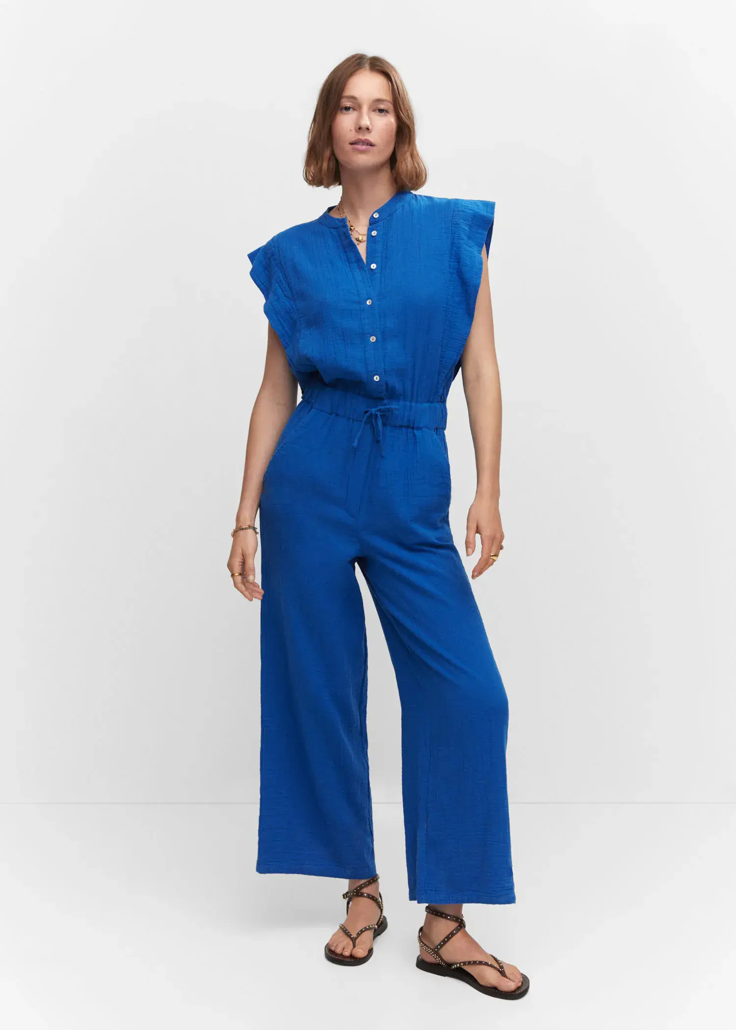 Mango Textured jumpsuit with button. a woman wearing a blue jumpsuit standing in front of a white wall. 