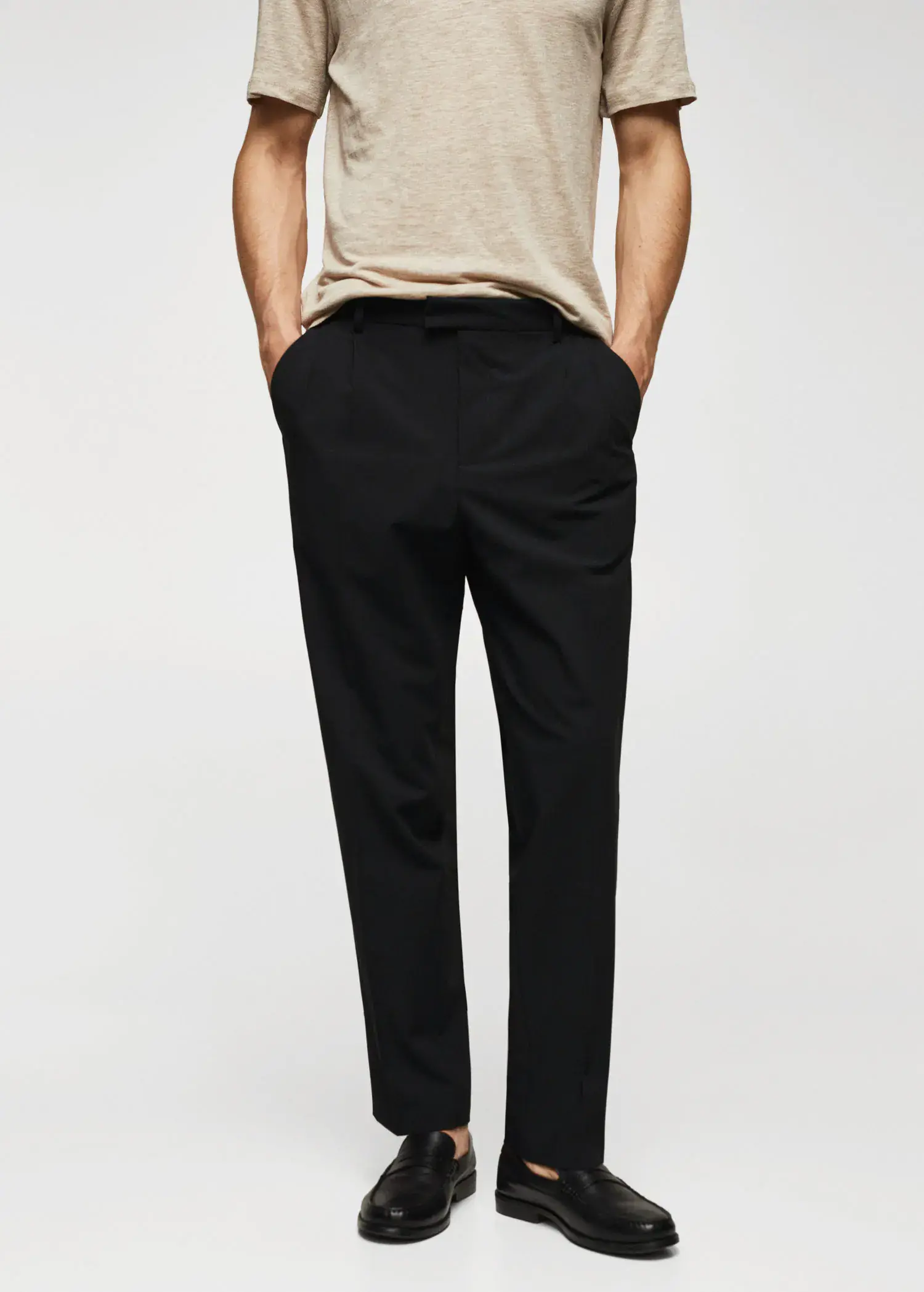 Mango Regular fit pleated cotton trousers. a man is standing with his hands in his pockets. 