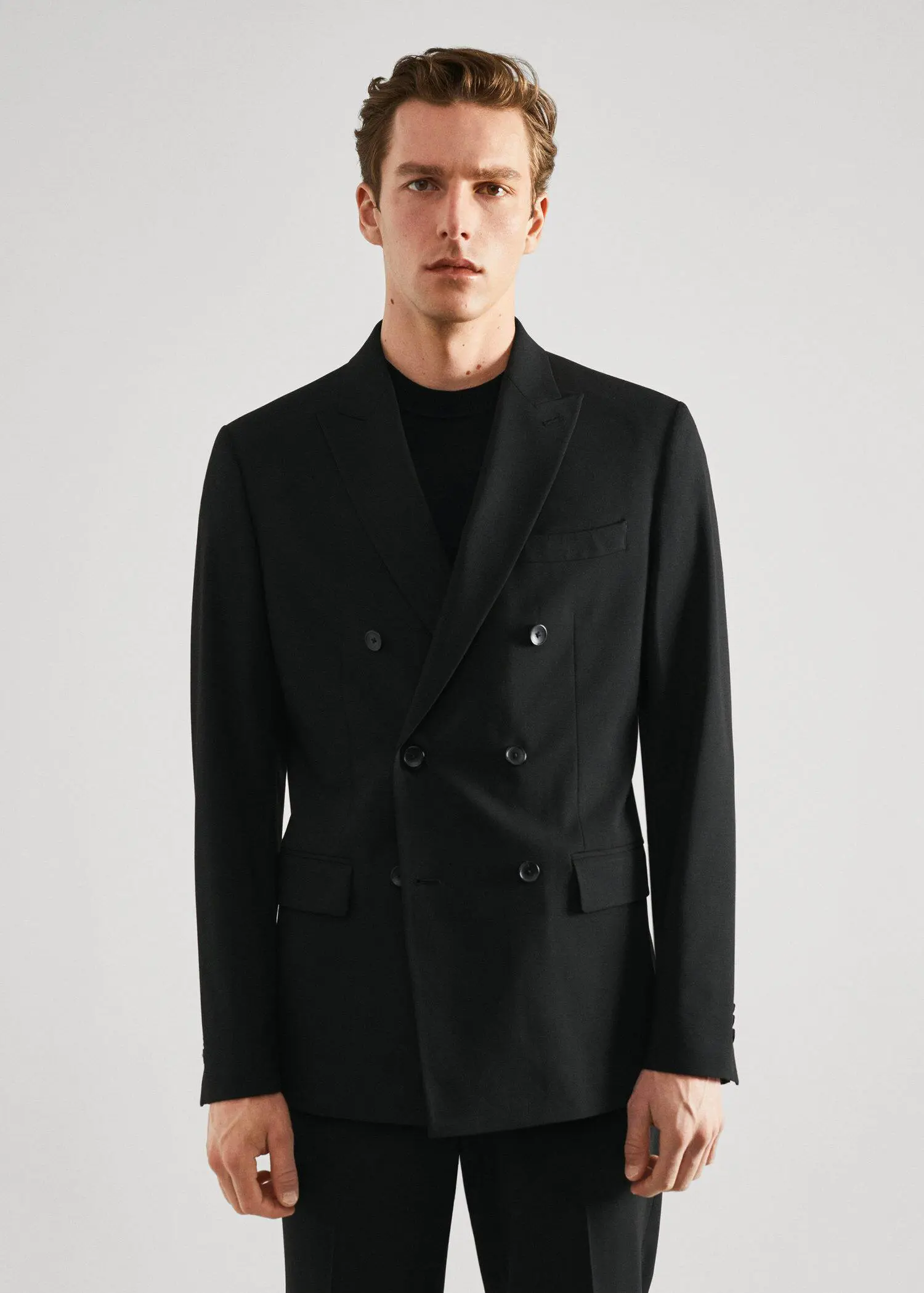 Mango Slim fit double-breasted suit blazer. a man wearing a black suit standing in front of a white wall. 