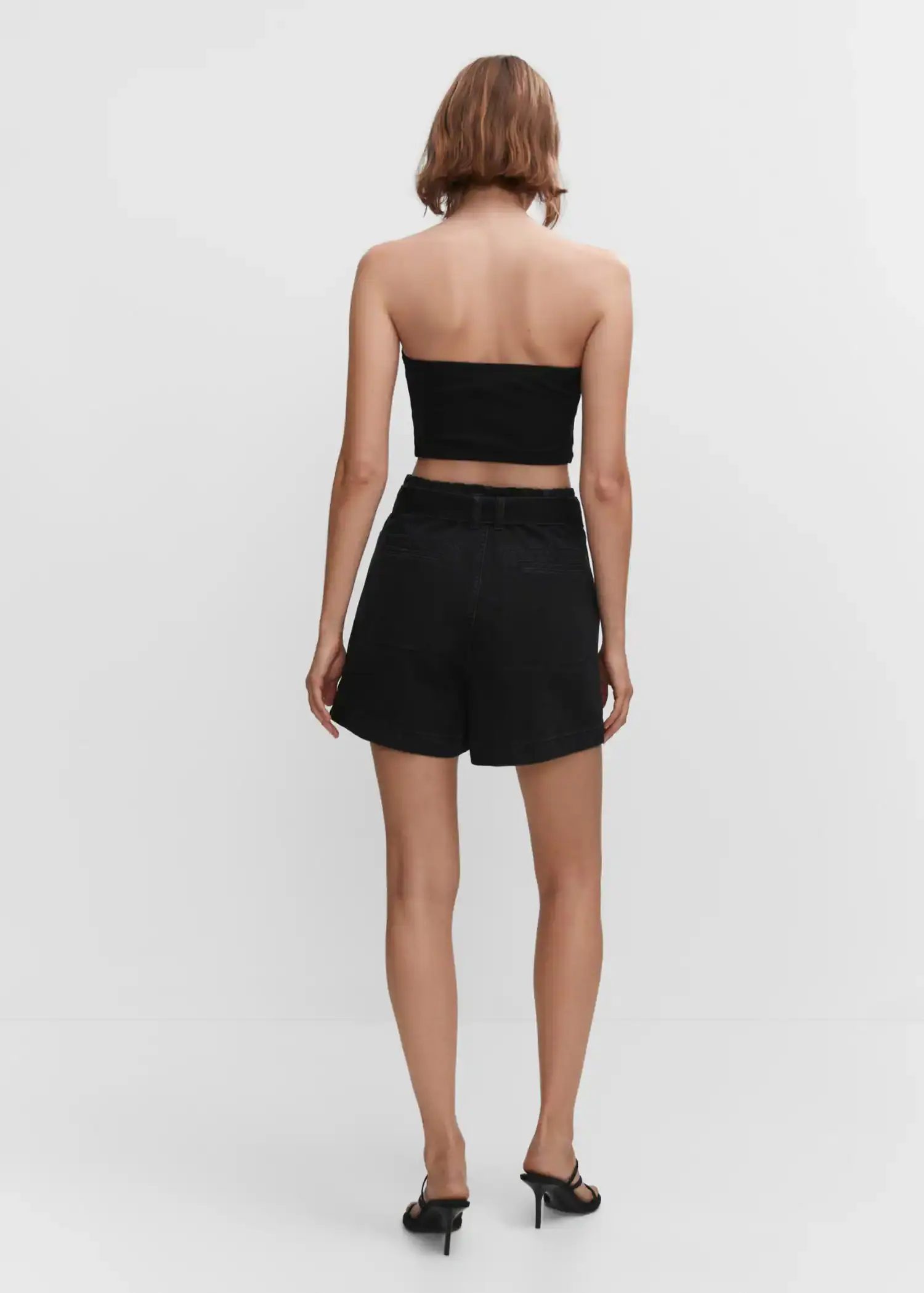 Mango Paperbag shorts with belt. a woman in a black outfit standing in front of a white wall. 