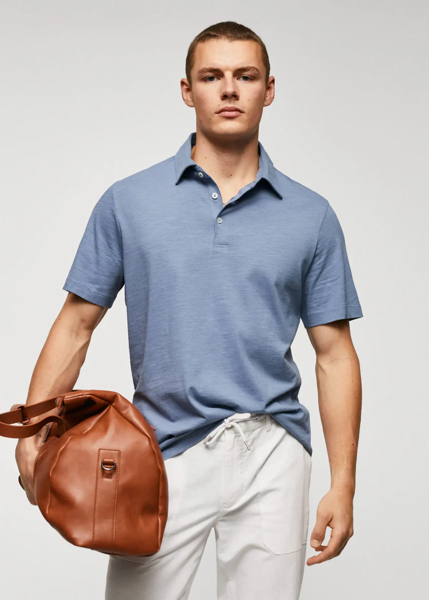 Mango 100% cotton basic polo shirt . a man holding a brown duffel bag in front of a white wall. 