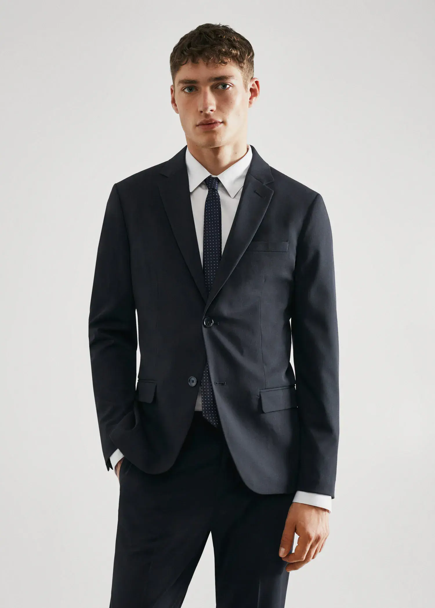 Mango Super slim-fit suit jacket in stretch fabric. a man in a suit and tie standing with his hands in his pockets. 