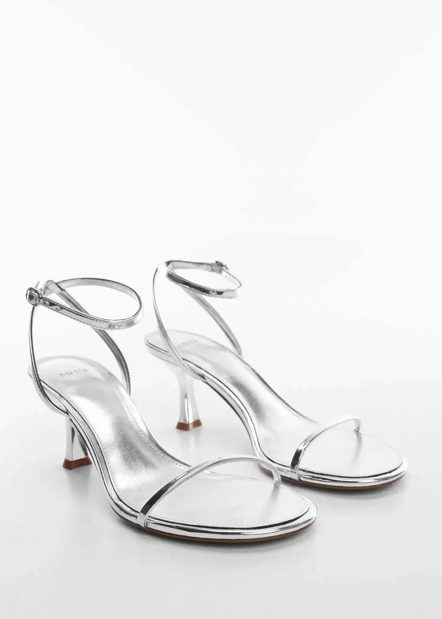 Mango Metallic heel sandals. a pair of shiny silver heels on a white surface. 
