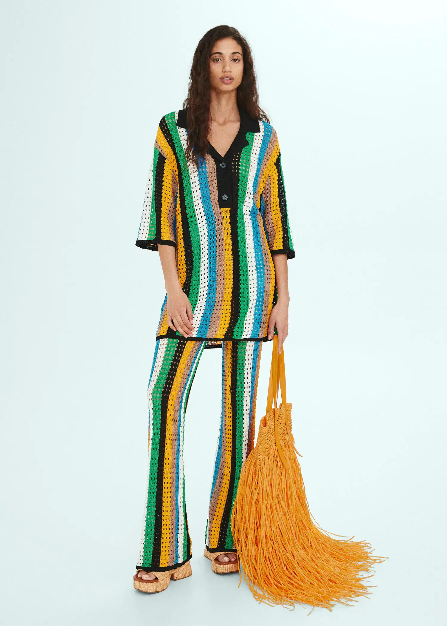 Mango Maxi fringed natural fibre bag. a woman in a colorful outfit standing next to a yellow bag. 