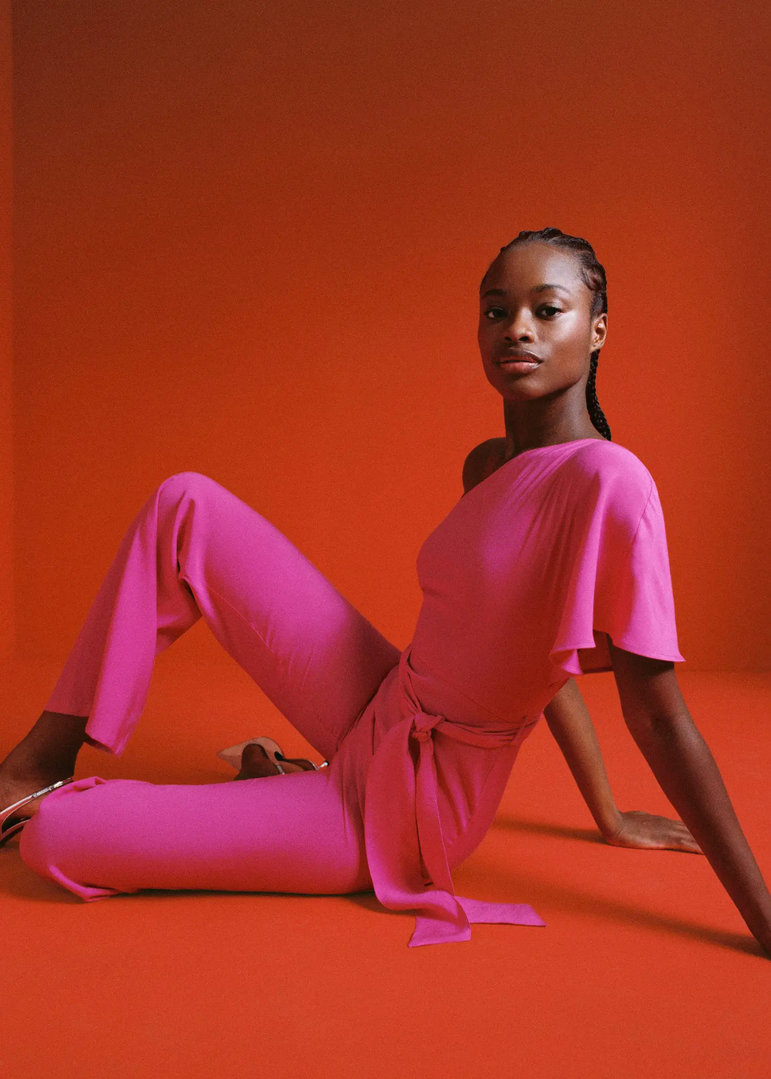 Mango Asymmetric long jumpsuit. a woman sitting on the ground wearing a pink outfit. 