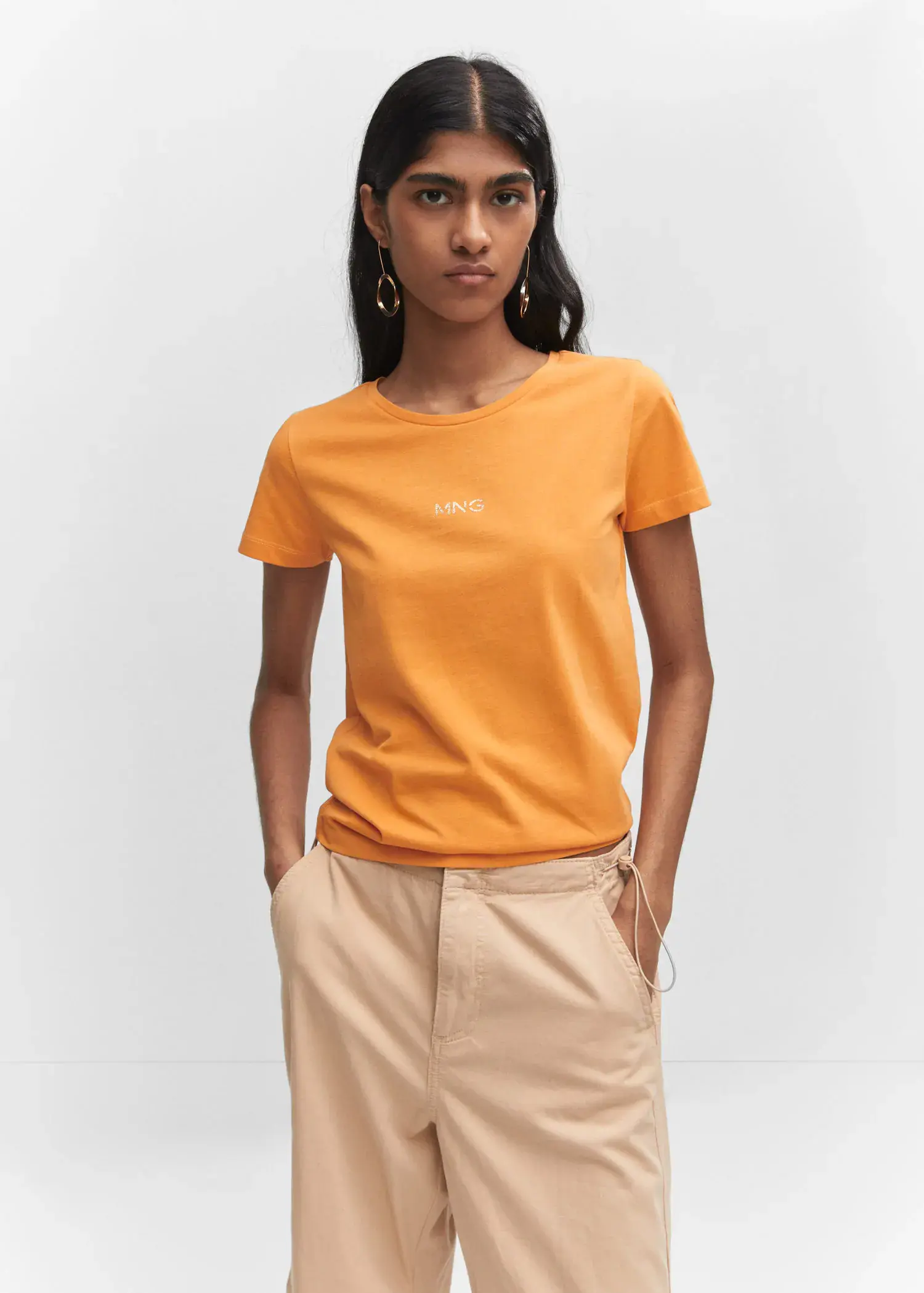 Mango Metallic logo T-shirt. a woman in a yellow t-shirt is standing with her hands in her pockets 