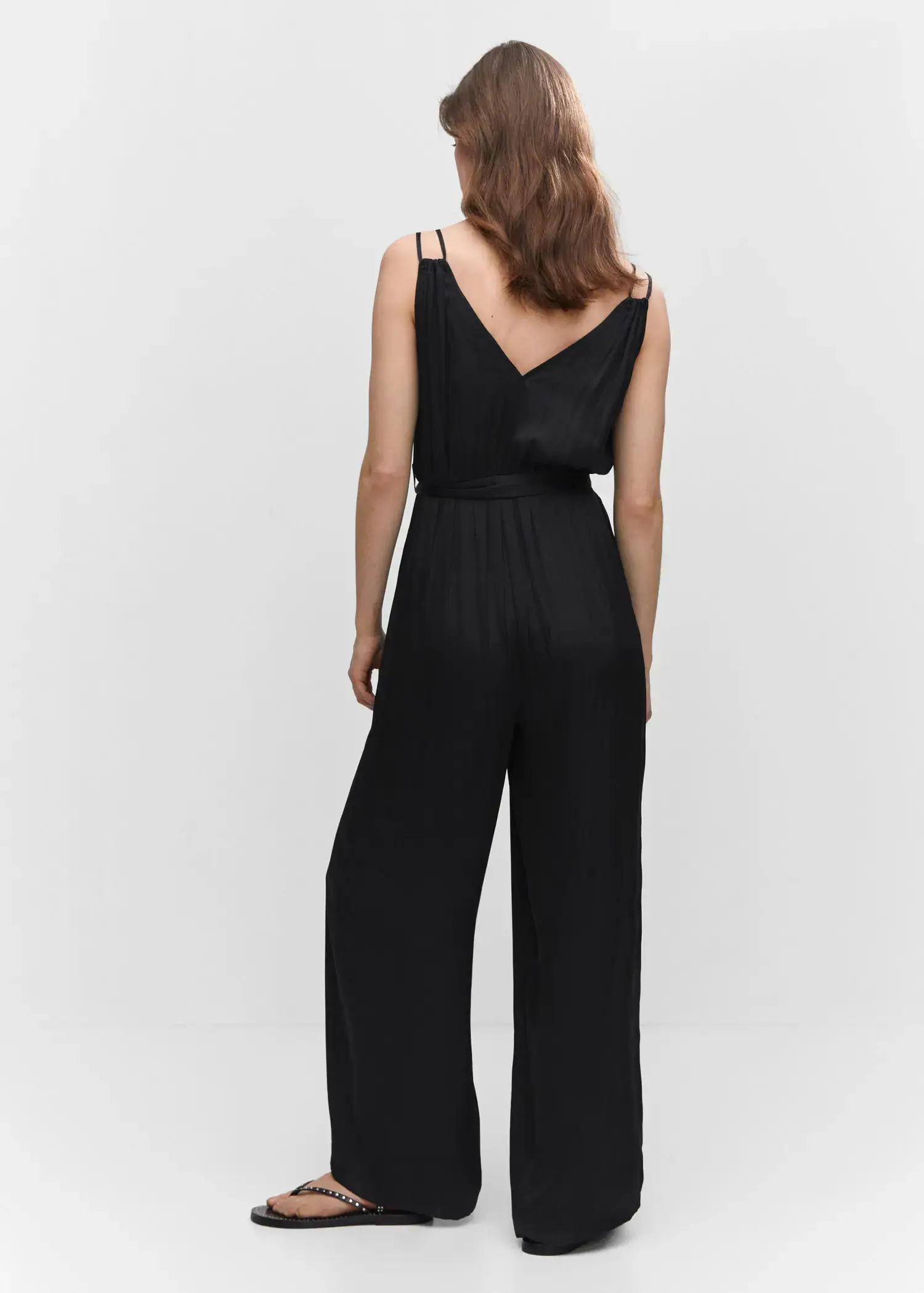 Mango Satin pleated jumpsuit. a woman in a black jumpsuit is standing in front of a white wall. 
