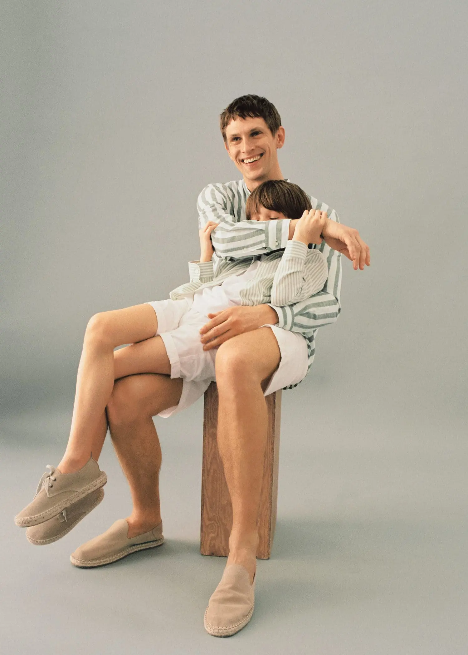 Mango KIDS/ Striped cotton dress shirt. a man sitting on top of a wooden block holding a child. 