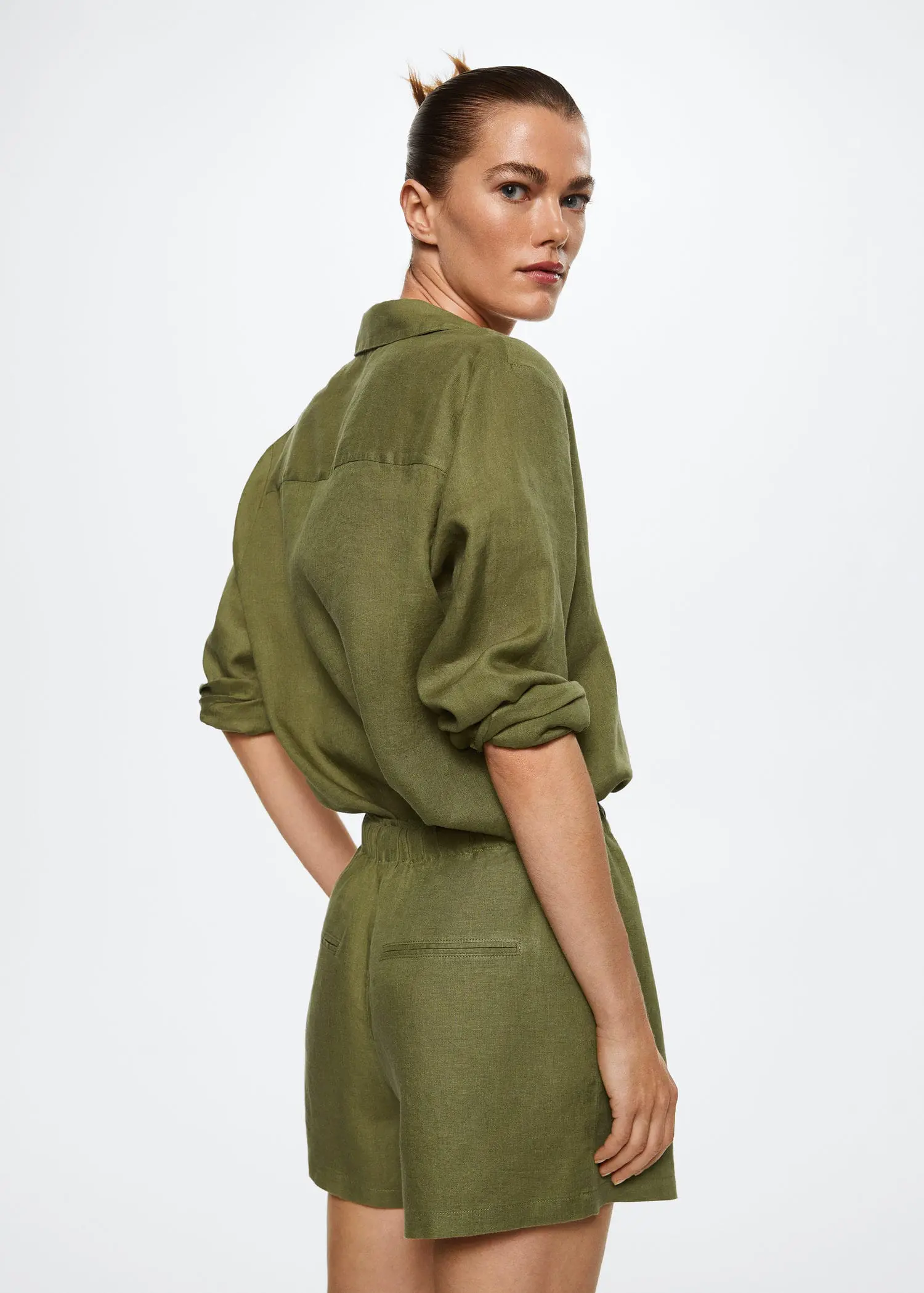 Mango 100% linen shorts. a woman in a green outfit is standing in front of a white wall. 