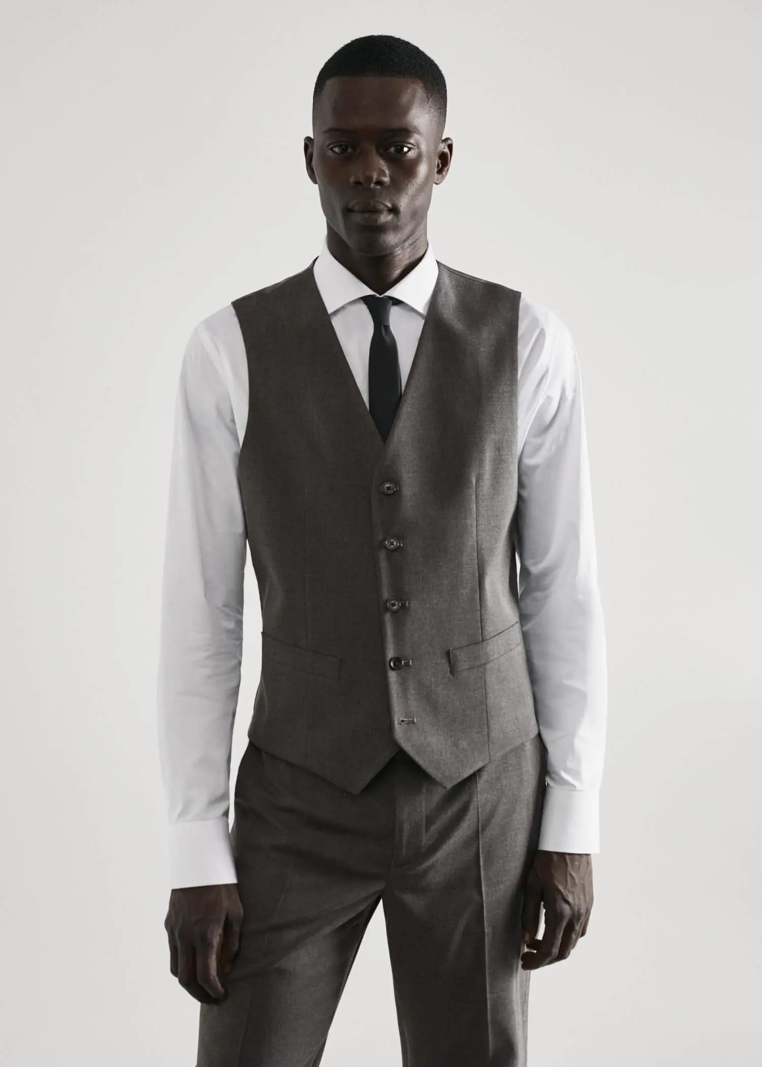 Mango Slim-fit suit vest. a man wearing a suit and tie standing in front of a white wall. 