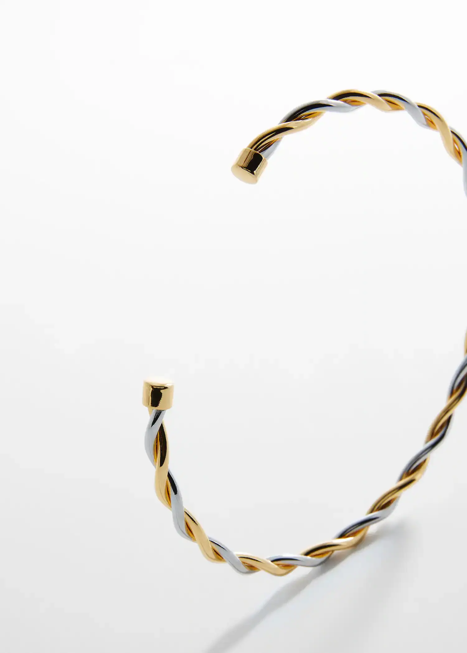 Mango Criss-cross rigid necklace. a close-up of a gold and silver bracelet on a table. 