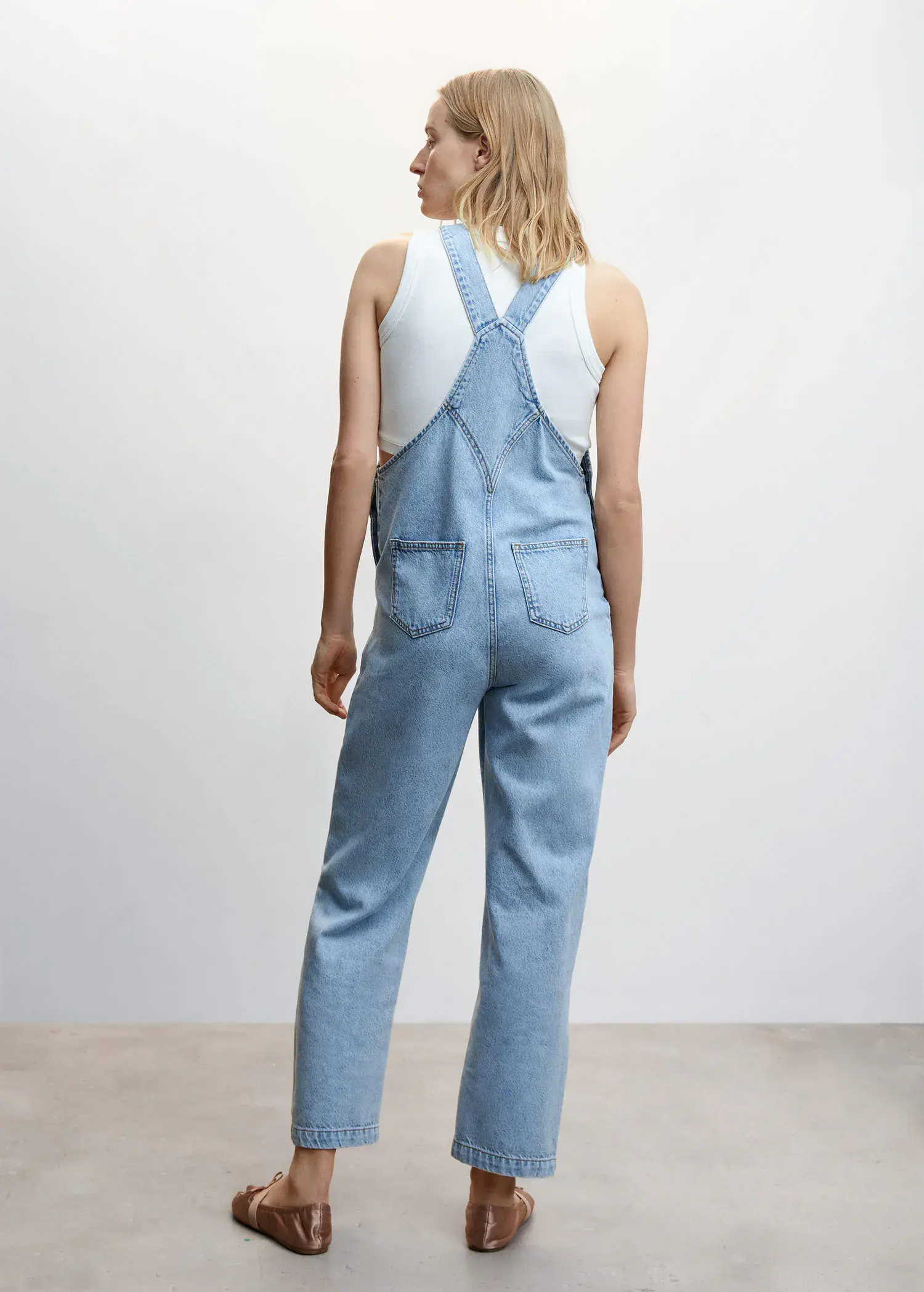 Mango Maternity denim dungarees. a woman wearing a blue overalls standing in front of a wall. 