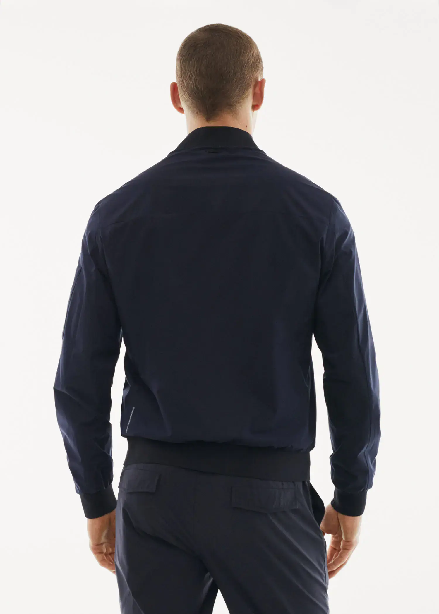 Mango Bomber jacket made of water-repellent technical fabric. a man wearing a black jacket standing in front of a white wall. 