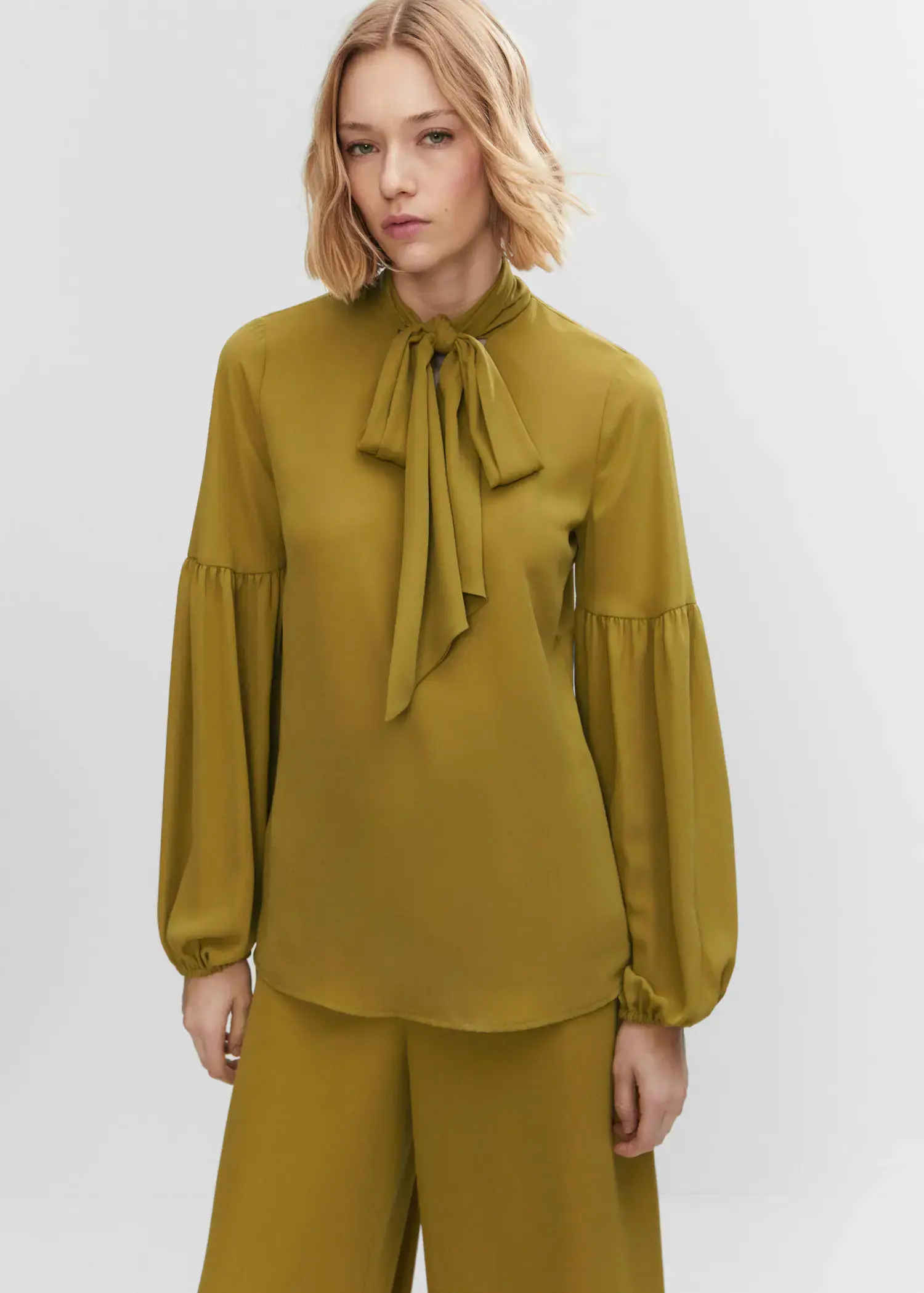 Mango Blouse with puffed sleeves and bow . a woman wearing a green blouse and a pair of pants. 