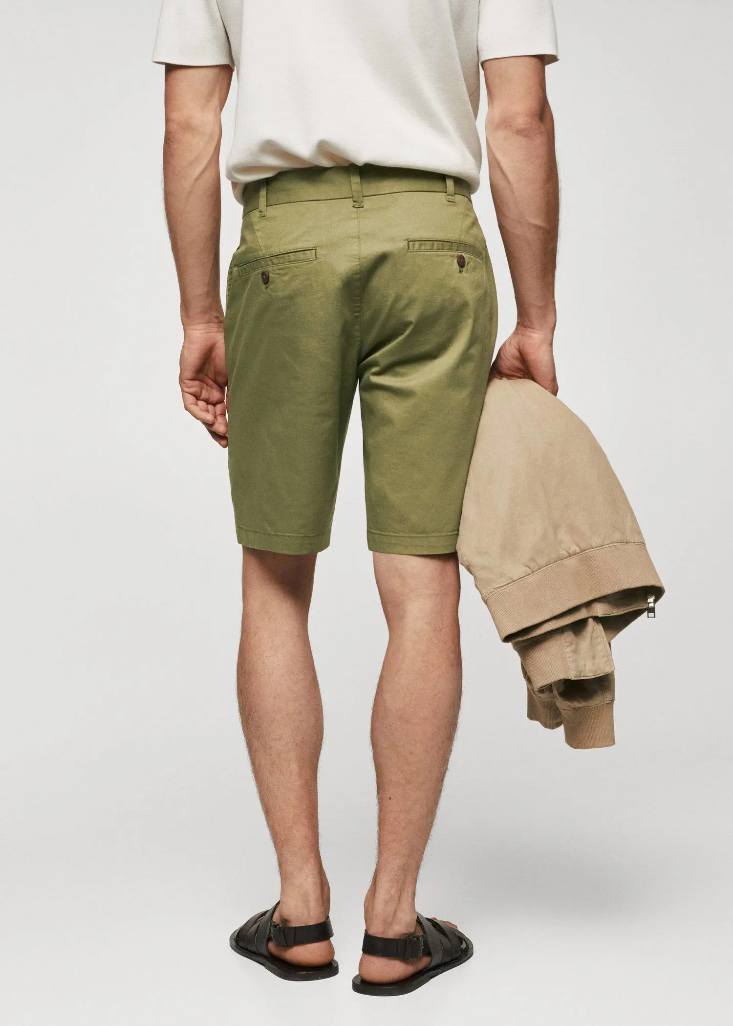 Mango Chino Bermuda shorts. a man wearing a pair of green shorts and holding a jacket. 