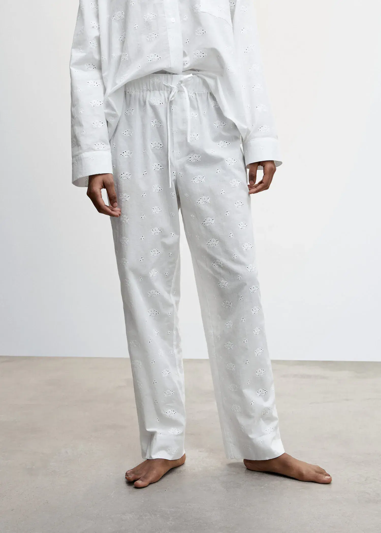 Mango Pajama pants with openwork details. a person standing in a room wearing white pajamas. 