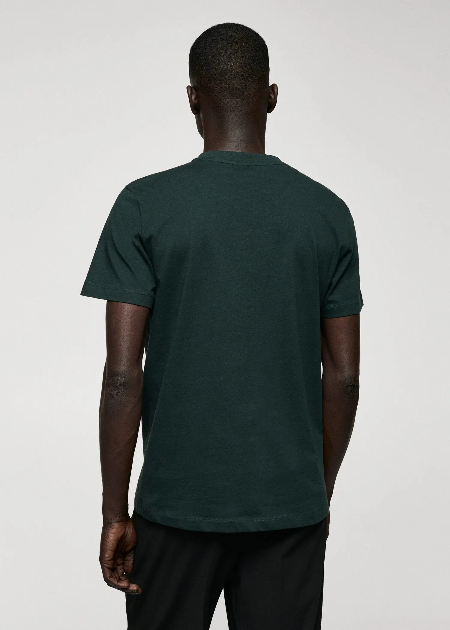 Mango Basic cotton V-neck T-shirt. a person wearing a green t-shirt standing in front of a white wall. 