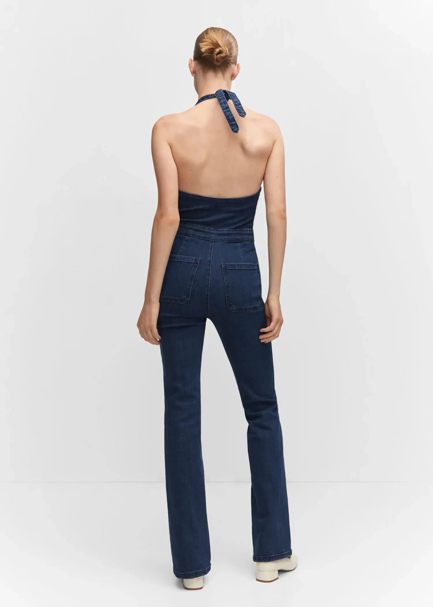 Mango Denim halter-neck jumpsuit. a woman in a blue jumpsuit is standing in front of a wall. 